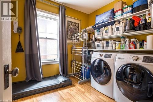 This room features hardwood-style flooring, a window providing natural light, and a dedicated laundry area with white front-loading machines - 36 Eastbourne Avenue, Hamilton, ON - Indoor Photo Showing Laundry Room