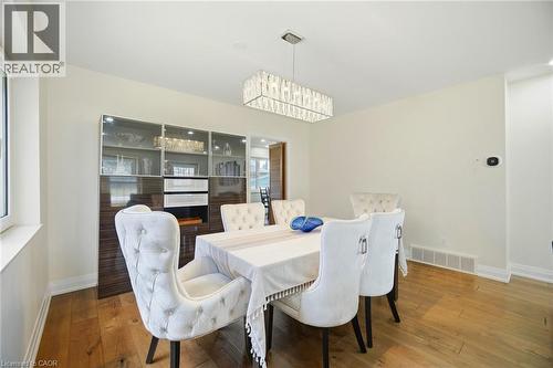 Dining area featuring hardwood floors, a modern rectangular chandelier, and a built-in display cabinet with glass doors - 38 Leclaire Street, Hamilton, ON - Indoor Photo Showing Dining Room