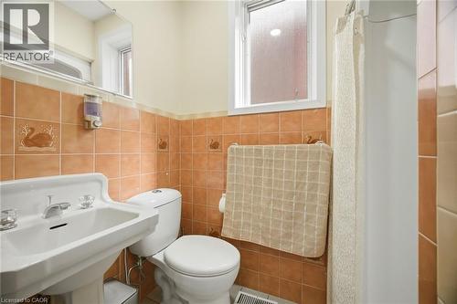 Bathroom featuring a white pedestal sink, toilet, and a tiled shower area with a shower curtain - 38 Leclaire Street, Hamilton, ON - Indoor Photo Showing Bathroom