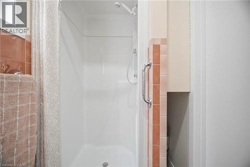 The bathroom features a shower with a handheld showerhead and a built-in grab bar, alongside peach-toned wall tiles - 38 Leclaire Street, Hamilton, ON - Indoor Photo Showing Bathroom