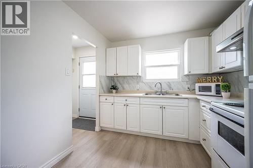 Bright kitchen featuring white cabinetry, light countertops, a stainless steel sink, and wood-finish flooring - 212 Westcourt Place, Waterloo, ON - Indoor Photo Showing Kitchen With Double Sink
