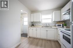 Bright kitchen featuring white cabinetry, light countertops, a stainless steel sink, and wood-finish flooring - 