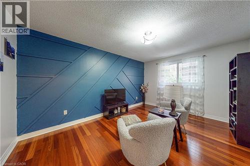 Living space featuring hardwood flooring, a statement wall with geometric detailing, and a window with sheer curtains - 24 Hildegard Drive, Hamilton, ON - Indoor