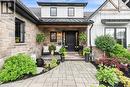 Stone and vertical siding exterior with black trim windows, a black paneled front door, covered porch with exposed wood beam, and a paved walkway - 253 Central Avenue, Grimsby, ON 