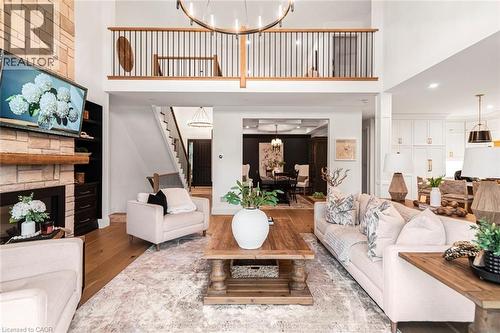 Open-concept living area featuring a two-story ceiling, stone fireplace with wood mantel, a second-story balcony with metal balusters, hardwood flooring, and recessed lighting - 253 Central Avenue, Grimsby, ON 