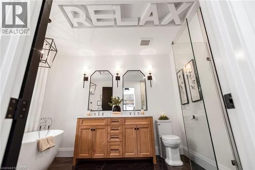 Contemporary bathroom featuring a freestanding soaking tub, wood-finish double vanity with stone countertop, frameless glass shower enclosure, and dark tile flooring - 253 Central Avenue, Grimsby, ON 
