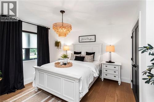 Bright bedroom featuring wood-finish flooring, a contemporary chandelier, a window with roller shade, and a black paneled door - 253 Central Avenue, Grimsby, ON 