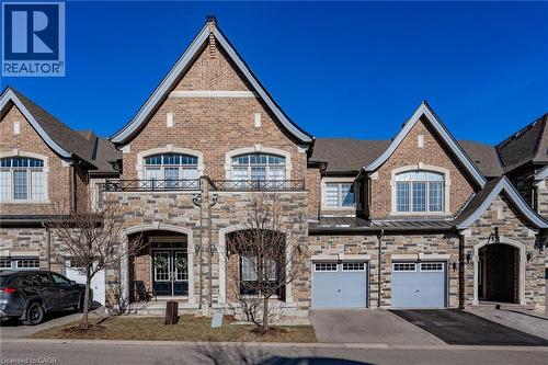 The property features an appealing exterior facade with a combination of brick and stone, a prominent front entrance, and two distinct garage doors - 2453 Village Common, Oakville, ON - Outdoor With Facade