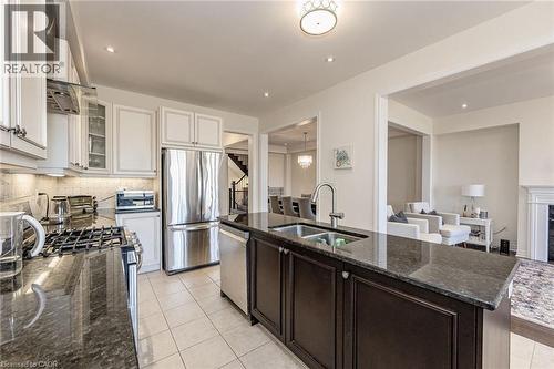 Well-appointed kitchen featuring a large island with an undermount sink, stainless steel appliances, white cabinetry, and dark granite countertops - 2453 Village Common, Oakville, ON - Indoor Photo Showing Kitchen With Stainless Steel Kitchen With Double Sink With Upgraded Kitchen