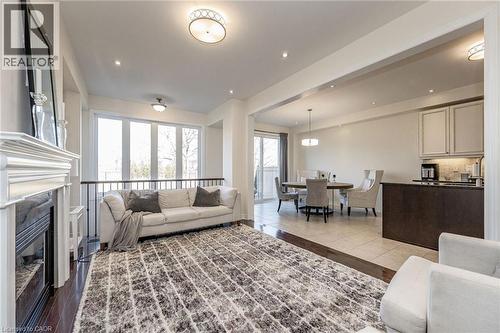 This open-concept living area features hardwood flooring, a fireplace with a white mantel, and large windows providing natural light - 2453 Village Common, Oakville, ON - Indoor Photo Showing Living Room With Fireplace