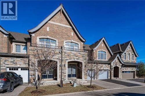 The property features a charming exterior with a combination of brick and stone cladding, prominent gables, and arched windows - 2453 Village Common, Oakville, ON - Outdoor With Facade