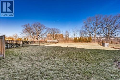 The property features an extensive yard with a lawn, mature trees, and a black metal fence - 2453 Village Common, Oakville, ON - Outdoor