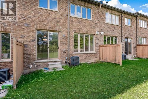 The property features a brick exterior with multiple windows and a sliding glass door leading to a private grassy area - 2453 Village Common, Oakville, ON - Outdoor With Exterior