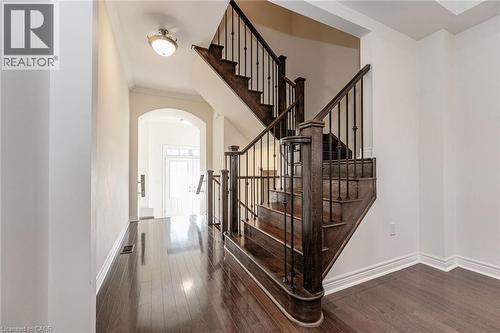 The property features rich hardwood floors, an elegant staircase with dark wood and wrought iron balusters, and an arched entryway - 2453 Village Common, Oakville, ON - Indoor Photo Showing Other Room