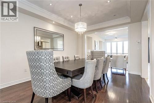 The dining area features dark hardwood floors, white walls, and a decorative chandelier - 2453 Village Common, Oakville, ON - Indoor Photo Showing Dining Room