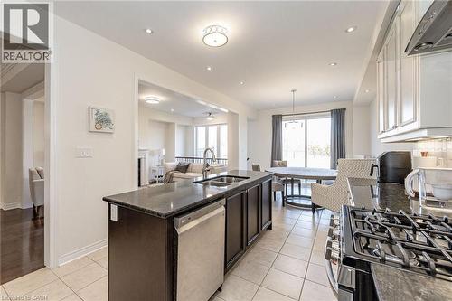 The kitchen features tile flooring, dark countertops, a gas range, and a stainless steel dishwasher - 2453 Village Common, Oakville, ON - Indoor Photo Showing Kitchen With Double Sink