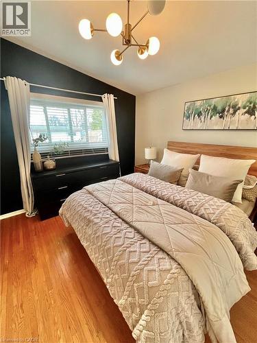 The room features warm-toned hardwood flooring, a window with blinds and curtains, and a modern ceiling light fixture - 241 Thorner Drive, Hamilton, ON - Indoor Photo Showing Bedroom