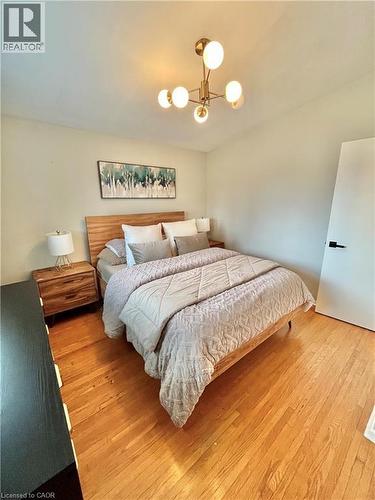 This room features hardwood flooring, a modern light fixture, and light-colored walls - 241 Thorner Drive, Hamilton, ON - Indoor Photo Showing Bedroom