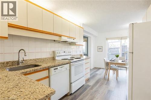 The kitchen features granite countertops, a stainless steel sink with a gooseneck faucet, white appliances including a stove and dishwasher, and light-colored cabinetry - 121 University Avenue E Unit# 102, Waterloo, ON - Indoor Photo Showing Kitchen