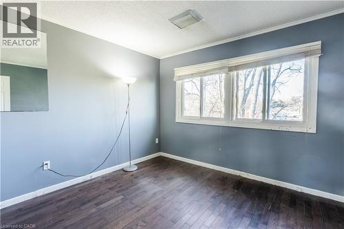 This room features dark hardwood flooring, light blue walls, and a large window with blinds that provides natural illumination - 121 University Avenue E Unit# 102, Waterloo, ON - Indoor Photo Showing Other Room