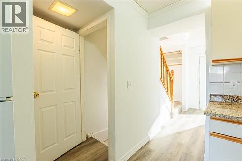 The property features a staircase with a wooden railing, light-colored flooring, and a kitchen area with white cabinetry, a tiled backsplash, and a granite-patterned countertop - 121 University Avenue E Unit# 102, Waterloo, ON - Indoor Photo Showing Other Room