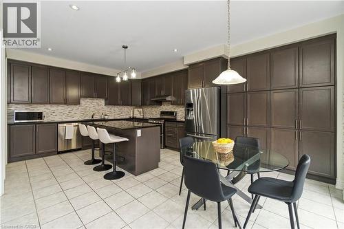 The kitchen features extensive dark cabinetry, a kitchen island with seating, stainless steel appliances, and tiled flooring - 4 Macbean Crescent, Waterdown, ON - Indoor