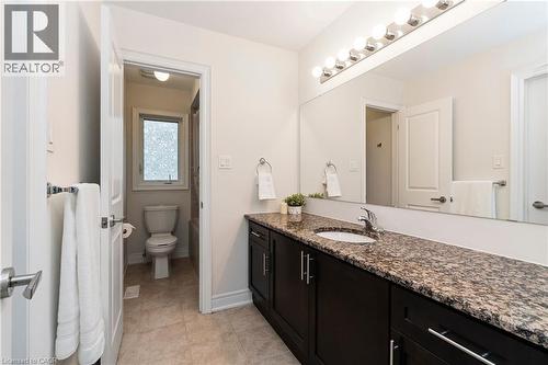 This bathroom features a dark wood vanity with a granite countertop and an integrated sink, complemented by a large mirror and overhead lighting - 4 Macbean Crescent, Waterdown, ON - Indoor Photo Showing Bathroom