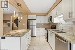 Kitchen with stainless steel appliances, light stone countertops, white cabinets, light tile patterned floors, and hanging light fixtures - 