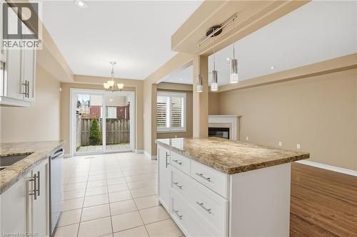 Kitchen featuring white cabinetry, a glass covered fireplace, light stone counters, stainless steel dishwasher, and a kitchen island - 91 Chamomile Drive, Hamilton, ON - Indoor Photo Showing Kitchen With Upgraded Kitchen