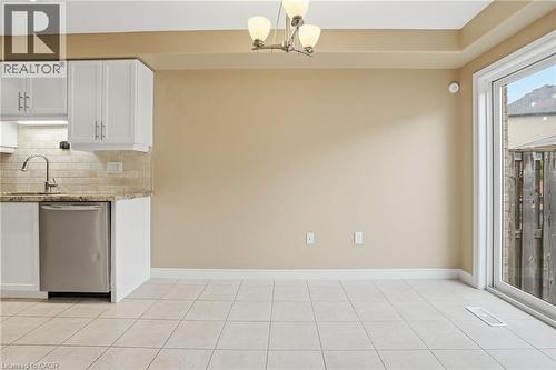 Kitchen featuring white cabinets, light stone counters, dishwasher, and tasteful backsplash - 91 Chamomile Drive, Hamilton, ON - Indoor Photo Showing Kitchen