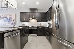 Well-appointed kitchen featuring dark wood cabinetry, granite countertops, and stainless steel appliances including a refrigerator, dishwasher, and range with an overhead hood - 