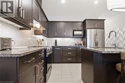 The kitchen features dark wood cabinetry, granite countertops, stainless steel appliances, and a tiled backsplash - 