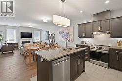 The open concept living area features a kitchen with dark cabinetry, granite countertops, and stainless steel appliances, including a dishwasher, stove, and range hood - 