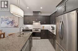 Kitchen featuring dark wood cabinetry, stainless steel appliances, granite countertops, and a white tile backsplash - 