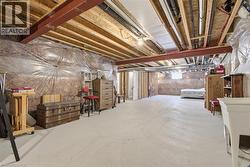 Expansive unfinished basement featuring exposed ceiling joists and support beams, with durable concrete flooring - 