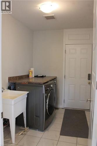 Laundry area featuring a utility sink, tiled flooring, and a solid exterior door - 40 Compass Trail, Cambridge, ON - Indoor Photo Showing Laundry Room