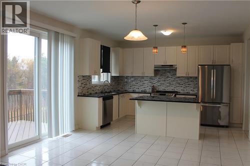 Bright kitchen featuring white cabinetry, a large center island with dark countertops, stainless steel appliances, and an intricate tile backsplash - 40 Compass Trail, Cambridge, ON - Indoor Photo Showing Kitchen With Stainless Steel Kitchen With Upgraded Kitchen