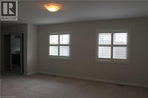 Carpeted interior space featuring two windows with white plantation shutters, a semi-flush mount ceiling light, and a mirrored closet door - 40 Compass Trail, Cambridge, ON - Indoor Photo Showing Other Room