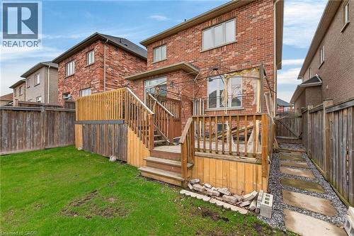 The property features a red brick exterior, a wooden deck with railing, and a grass lawn - 44 Matteo Trail, Hamilton, ON - Outdoor With Deck Patio Veranda
