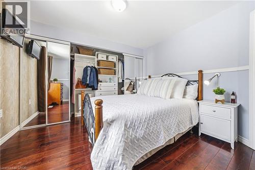 Bedroom featuring hardwood flooring, a bed with a black metal and wood frame, a white nightstand, and a closet with mirrored sliding doors - 30 Grand Avenue, Caledonia, ON - Indoor Photo Showing Bedroom