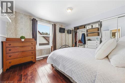 This bedroom features dark hardwood floors, a large window providing natural light, and a built-in closet system with shelving and hanging space - 30 Grand Avenue, Caledonia, ON 
