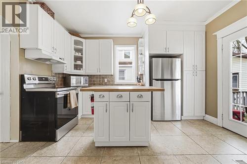 The kitchen features white cabinetry, a stainless steel refrigerator, an electric range, and a central island with a wooden countertop - 30 Grand Avenue, Caledonia, ON - Indoor Photo Showing Kitchen