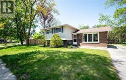 The property features a brick and siding exterior with a pitched roof, a front door with a storm door, and a well-maintained lawn with mature trees - 