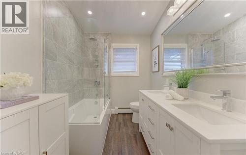 Bathroom featuring a double vanity with white cabinets and a white countertop, a large mirror, a bathtub with a glass shower screen, and tiled walls in the shower area - 400 Manchester Road, Kitchener, ON - Indoor Photo Showing Bathroom