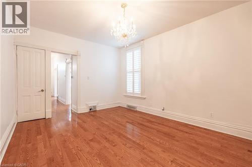 This living area features polished hardwood flooring, white walls, and a decorative chandelier - 198 Bay Street N, Hamilton, ON - Indoor Photo Showing Other Room