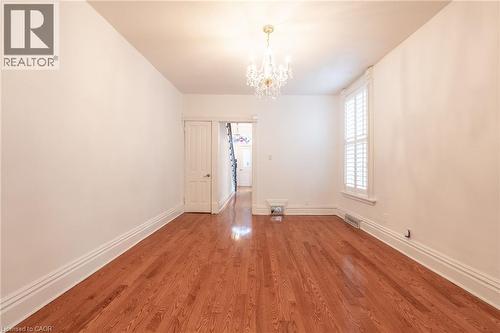 The living area features hardwood floors, a chandelier, and a window with white shutters - 198 Bay Street N, Hamilton, ON - Indoor Photo Showing Other Room