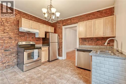 The kitchen features exposed brick walls, stainless steel appliances, tiled flooring, light wood cabinetry, and granite countertops - 198 Bay Street N, Hamilton, ON - Indoor Photo Showing Kitchen With Double Sink