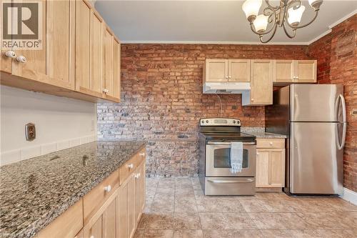 The kitchen features exposed brick walls, wood cabinetry, granite countertops, and stainless steel appliances - 198 Bay Street N, Hamilton, ON - Indoor Photo Showing Kitchen