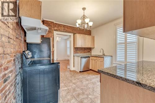 The kitchen features light wood cabinetry, granite countertops, a tiled backsplash, and an exposed brick wall - 198 Bay Street N, Hamilton, ON - Indoor