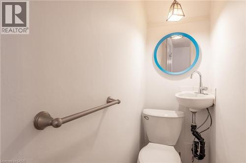The bathroom features a toilet, a wall-mounted sink with a chrome faucet, a round mirror with a blue frame, and a bronze-toned towel bar - 198 Bay Street N, Hamilton, ON - Indoor Photo Showing Bathroom